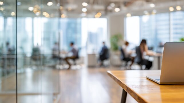 Office environment with laptop on desk and blurred workers creating a productive modern workspace