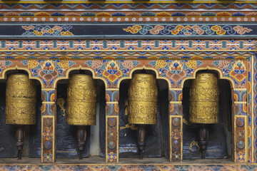 Gangtey Monastery, Bhutan - 20 September 2025: View of golden prayer wheels glimmering against the dark stone, framed by intricate, colorful carvings.