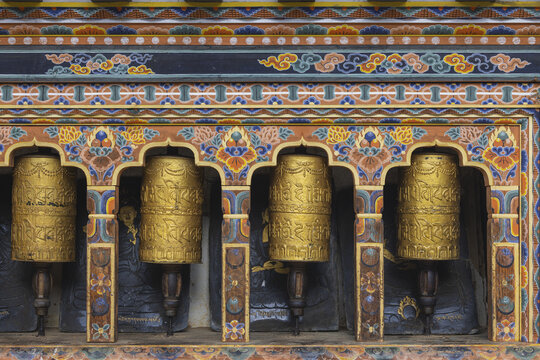 Gangtey Monastery, Bhutan - 20 September 2025: View of golden prayer wheels glimmering against the dark stone, framed by intricate, colorful carvings.