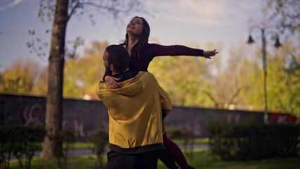 A joyful young couple shares moments of pure happiness, embracing and laughing together during a playful stroll in a vibrant park.