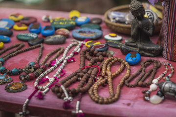 View of colorful stones, wooden beads, necklaces, and a small Buddha statue are displayed on a red table, Sopsokha, Punakha, Bhutan.