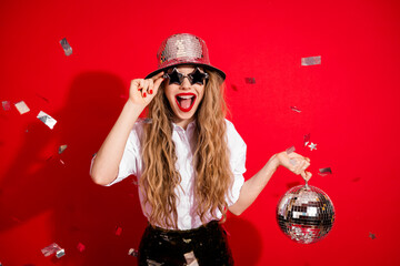 Chic woman with long blonde hair celebrating with disco ball in hand and festive confetti on...