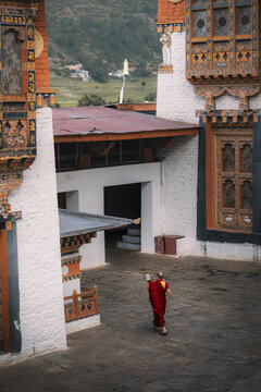 Punakha, Bhutan - 19 September 2025: View of a solitary monk in vibrant robes walks across the stone courtyard of Punakha Dzong, framed by the intricate architecture and whitewashed walls.