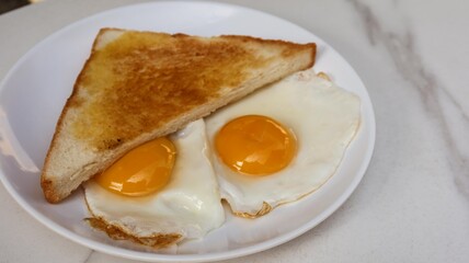 close up of a toast bread and two fried sunny side up eggs for breakfast on a white plate with copy space