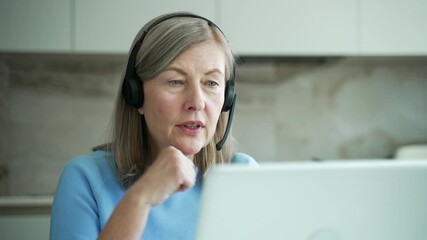 Confident senior female businesswoman in headset talking on a video call using laptop sitting in home office. Elderly woman entrepreneur has a business meeting. Coach speaks at online course. Close up - Powered by Adobe