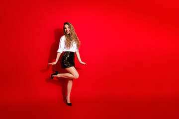 Elegant young woman posing confidently in glamorous attire against vibrant red background