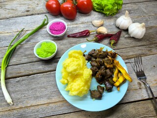 Chicken hearts with mashed potatoes on a plate surrounded by greens and vegetables. Restaurant food. Food style and serving dishes in a restaurant.