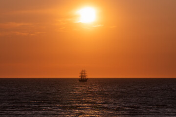 Silhouette of a three-masted tall ship sailing on the Baltic Sea horizon in Estonia against a dramatic golden orange sunset