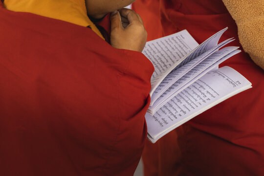 View of a person in vibrant red robes absorbed in the delicate pages of a book filled with intricate script, Wolakha Nunnery, Punakha, Bhutan.