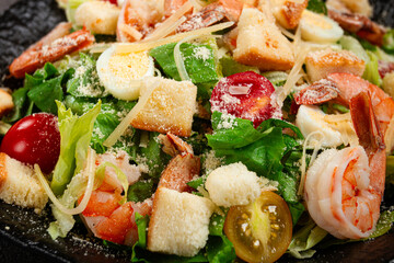caesar salad with tiger prawns, shrimp salad, lettuce leaves, quail eggs, cherry tomatoes, parmesan cheese, on a black plate,