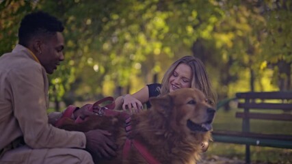 A diverse young couple shares a heartwarming moment, smiling and laughing as they lovingly pet their large brown dog in a vibrant autumn park. - Powered by Adobe