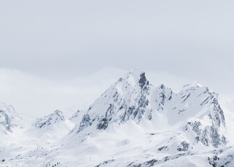 Fototapeta premium Sharp snow-covered mountain peak under soft winter light with dramatic ridges and surrounding snowy terrain