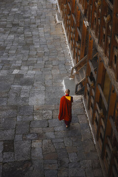 Trongsa, Bhutan - 22 September 2025: View of a monk in vibrant red robes walking along the grey stone path beside the intricately carved walls of Trongsa Dzong.