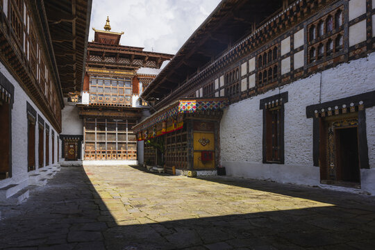View of sunlight casting shadows on the stone courtyard surrounded by white walls and ornate wooden balconies of a traditional Bhutanese building, Trongsa, Bhutan.