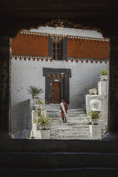 Trongsa, Bhutan - 22 September 2025: View of a lone figure ascending white stone steps towards an ornately decorated building, terracotta and white facade contrasting with the dark doorway.