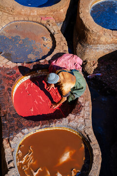 Person in vivid attire working with dye pits at a traditional tannery in a vibrant scene. Fez, Fez-Meknes, Northern Inland Morocco
