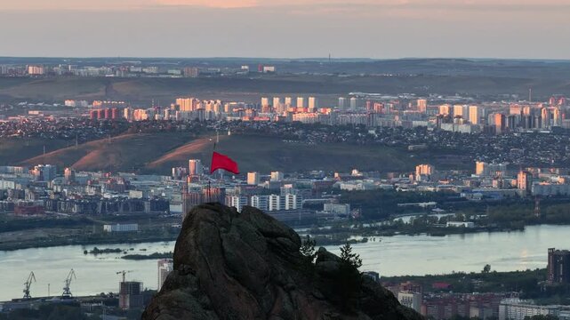 Red flag waving on mountain peak overlooking cityscape