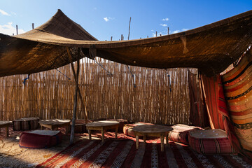 Traditional desert tent with wooden tables and colorful cushions under a clear blue sky. Agafay Desert, Marrakesh-Safi, Morocco