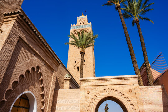 Tall minaret tower with palm trees under a vibrant blue sky in a historic architectural setting. Marrakesh, Morocco
