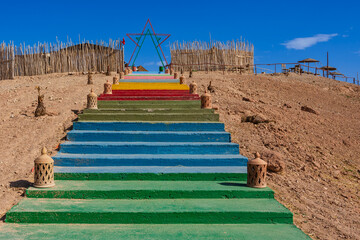 Colorful stairs leading to a star frame, bordered by rustic fences in a desert setting. Agafay Desert, Marrakesh-Safi, Morocco