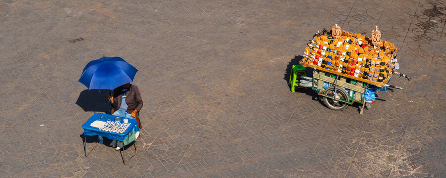 Aerial view of a street vendor with a blue umbrella and colorful cart on a paved street. Marrakesh, Morocco