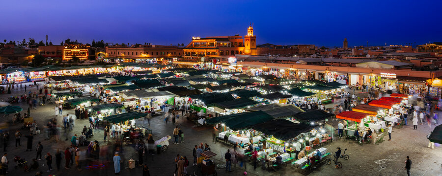 Lively evening market with illuminated stalls and bustling crowds under a deep blue sky. Marrakesh, Morocco