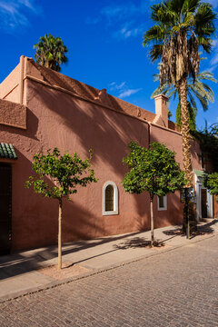 Sunlit adobe building with trees lining a cobblestone street under a clear blue sky. Marrakesh, Morocco