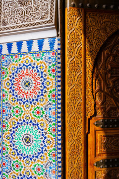Ornate wooden door beside vibrant geometric mosaic tile pattern with intricate designs. Marrakesh, Morocco