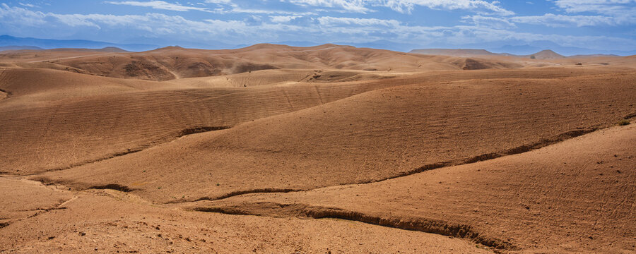 Arid desert landscape with rolling sand dunes under a partly cloudy blue sky. Agafay Desert, Marrakesh-Safi, Morocco