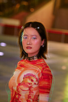 Woman in vibrant attire with projected geometric pattern on face stands in urban setting. Shanghai, China