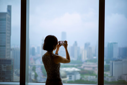 Woman taking a photo of a city skyline through a large window on a cloudy day. Shanghai, China 