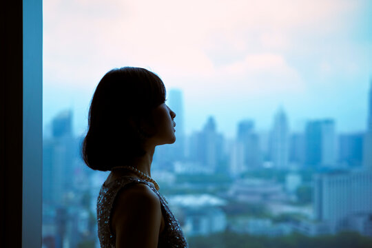 A woman in silhouette gazes out at a cityscape from a high vantage point at dusk. Shanghai, China 