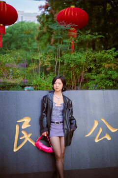 Woman in a fashionable outfit stands by a wall with Chinese characters, lanterns overhead. Shanghai, China 