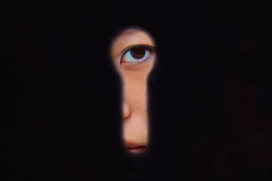 A young woman's eye visible through a dark keyhole, creating a mysterious and curious look. Shanghai, China