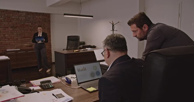Multigenerational business associates collaborate on a project in the office. They analyze data, discuss strategies, and work together towards a common goal.