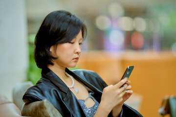 Woman in a leather jacket focuses on her smartphone while seated indoors. Shanghai, China