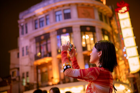 Woman in bright attire takes photo at night in a vibrant urban setting. Shanghai, China