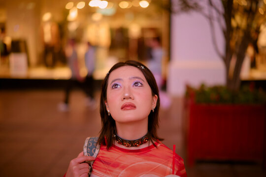 Woman in red shirt gazes upwards in a softly lit shopping mall setting. Shanghai, China