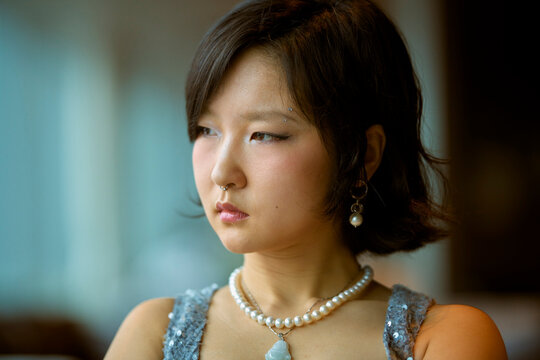 Young woman with bob haircut and pearl accessories gazes thoughtfully to the side. Shanghai, China