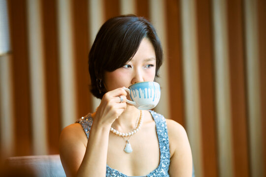 Woman in a sparkly top sips from a blue mug against a wooden striped background. Shanghai, China 