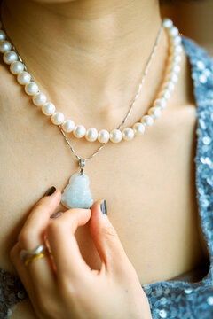 Close-up of a person holding a blue Buddha pendant on a pearl necklace with a sequin top. Shanghai, China 