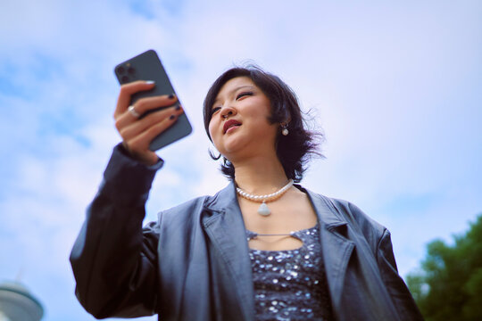 Woman with smartphone looks up at the sky wearing a black leather jacket. Shanghai, China