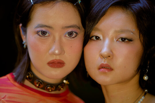 Two women with short black hair and bold makeup pose closely, wearing accessories and earrings. Shanghai, China 