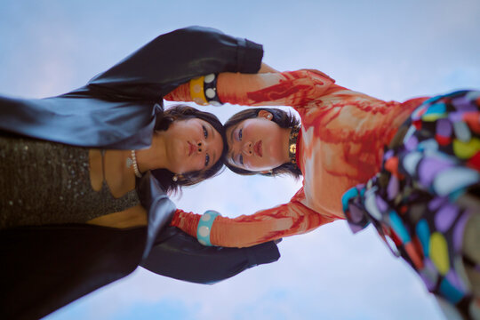 Two people in vibrant clothing hold hands against a blue sky, looking upwards. Shanghai, China