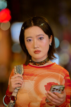 Young woman with short hair holds a phone, wearing a bright orange top and star hair clips. Shanghai, China