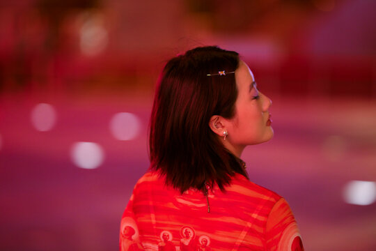 Woman in a red dress with short hair stands in soft pink lighting, facing sideways. Shanghai, China