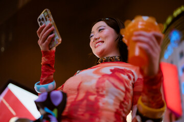 Smiling young woman holding a smartphone and a drink in a vibrant, colorful setting. Shanghai, China