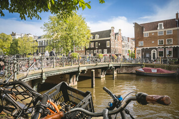 Bikes line a canal bridge in a sunny, vibrant Amsterdam street scene with historic buildings. Amsterdam,. Netherlands