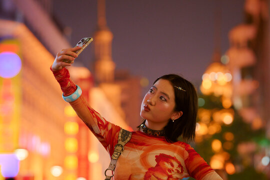 Young woman takes a selfie in vibrant, brightly lit city street at night. Shanghai, China