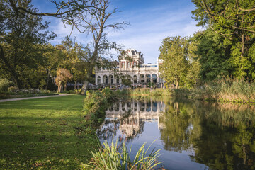 Grand white building surrounded by lush greenery and a reflective pond under a blue sky. Amsterdam,. Netherlands